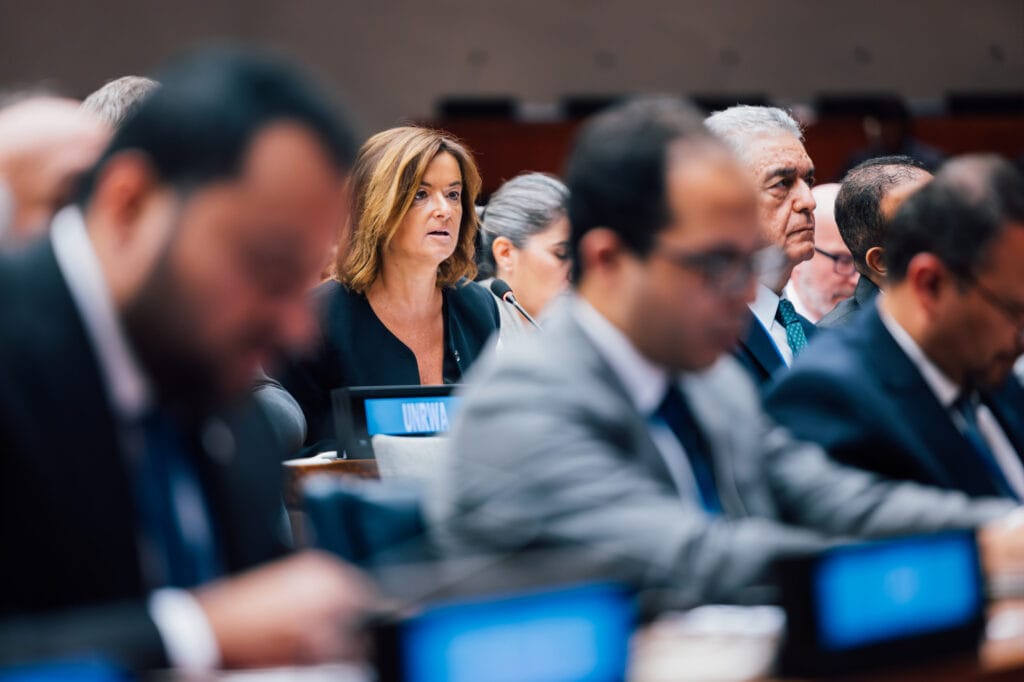 Zunanja ministrica Fajon sedi za mizo v dvorani in govori v imenu Slovenije. Okrog nje drugi ljudje, slika od daleč.