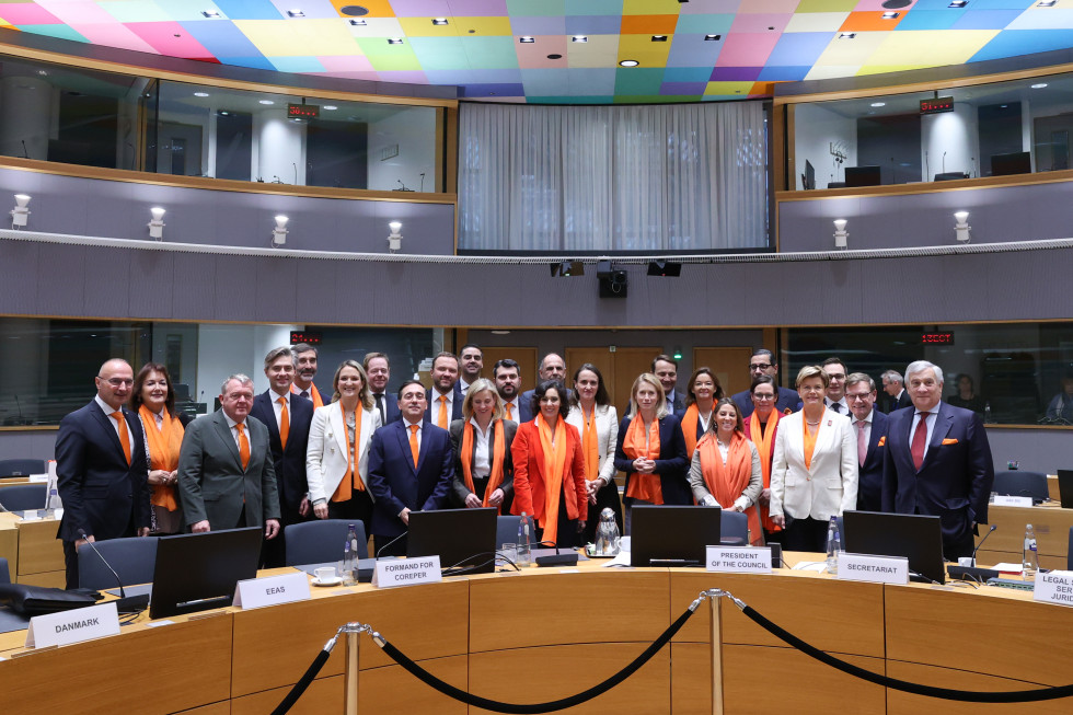 Skupina zunanjih ministrov EU stoji v dvorani in pozira za skupinsko fotografiranje. Vsak od njih nosi nekaj oranžnega.